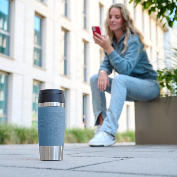 Blauer Thermobecher mit Frau im Hintergrund